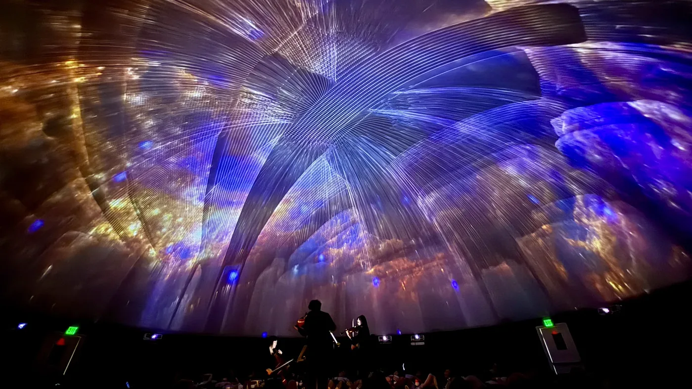 Light spread across the whole curved dome ceiling, with the string players silhouetted below.
